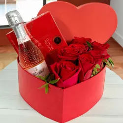 Rosas rojas en caja con forma de corazón y bombones.